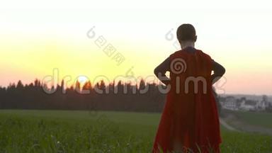 日落时穿着超级英雄斗篷的男孩站在田野里